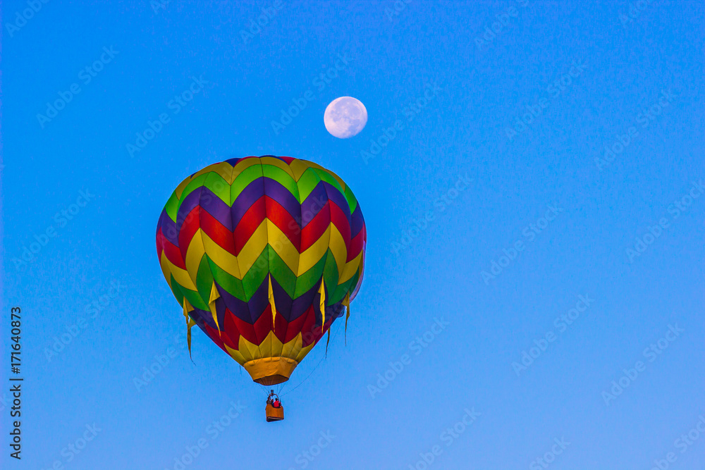 Fototapeta premium Bright Hot Air Balloon In Early Morning With Moon Still Showing