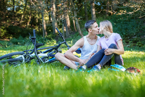 Young happy couple in love kissing. Walking in the park on bicycles. The concept of cycling and a healthy lifestyle and love.
