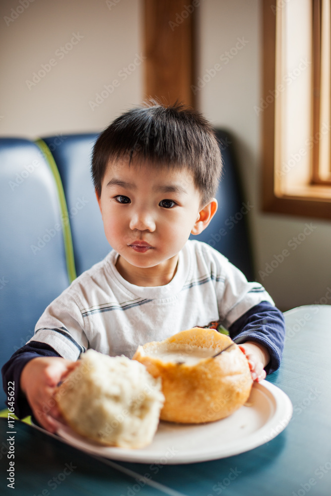 Asian boy eating clam chowder in a bread bowl Asian boy eating clam chowder in a bread bowl