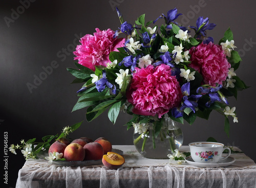 Bouquet of peonies, irises and Jasmine in the jar and the peaches on the table.