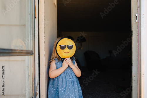 Toddler girl with a happy smiley emoticon face in front of her face.