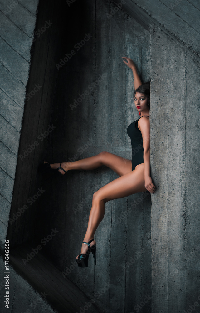  Fashion portrait of a young girl in black bikini and black shoes. Grey geometric abstract background