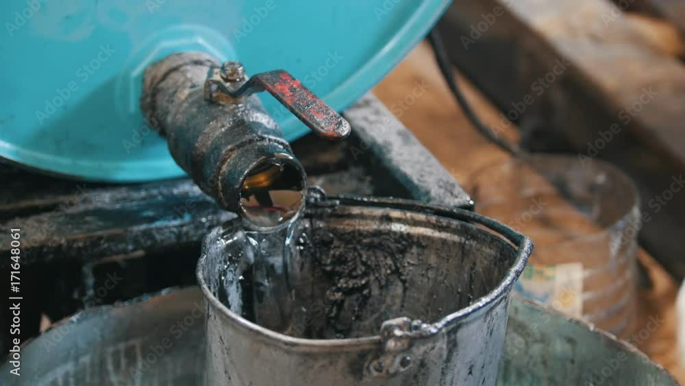 Worker pours engine oil or chemical liquid into the old scratched bucket Worker pours engine oil or chemical liquid into the old scratched bucket