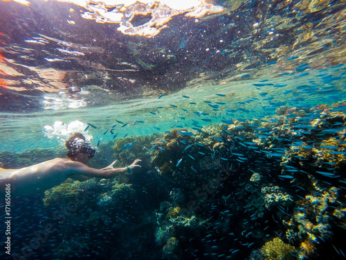 Young boy Snorkel swim in shallow water with coral school of fis