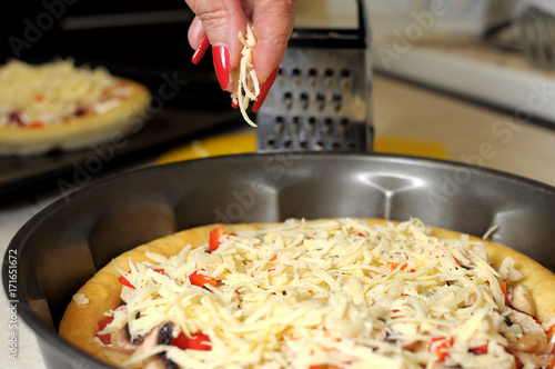 A female hand sprinkles a pizza with grated cheese close-up.