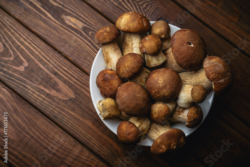 Fresh porcini mushrooms in a plate on wooden table, overhead or top view