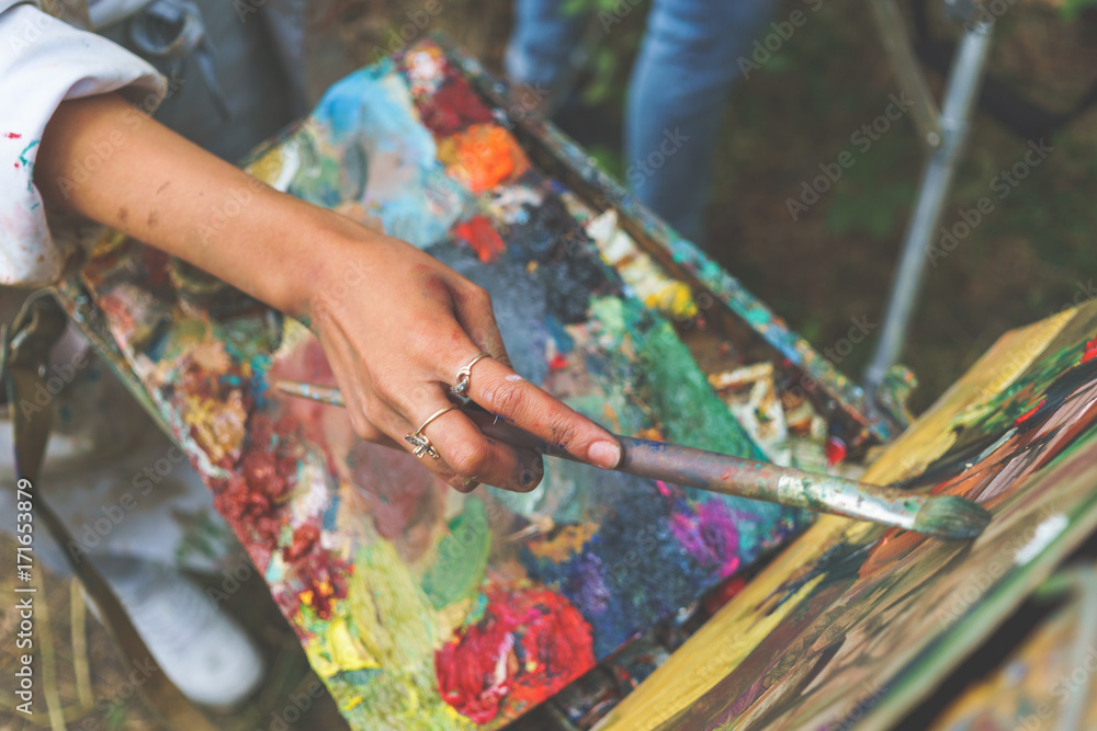 Closeup of female artist hand paint a picture on a palette at workshop, close up top view Closeup of female artist hand paint a picture on a palette at workshop, close up top view