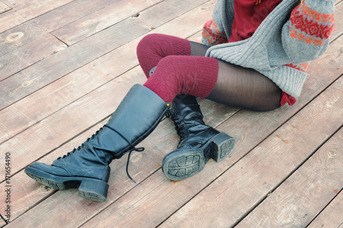 Female legs dressed in knee high boots and knitted stockings, woman sitting on a wooden planking photo