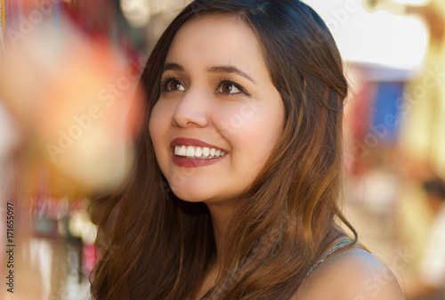 Close up of a beautiful smiling young woman looking a colorful andean traditional art, in colorful market fabrics background