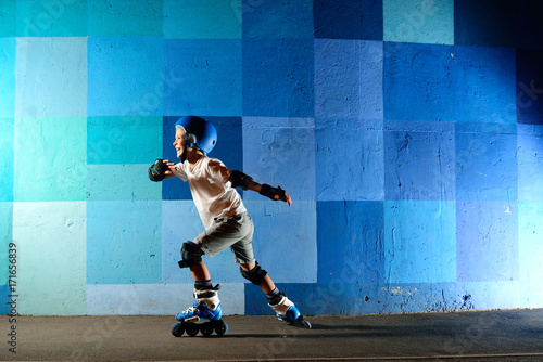 Cute little boy on roller skates running against the blue graffiti wall