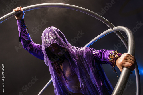 Fairy-tale character assassin in a purple cloak with a hood with two large cross wheel