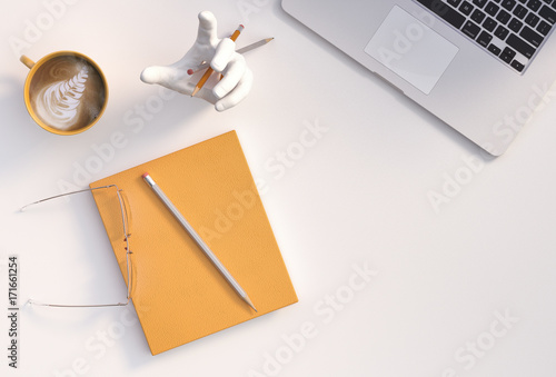 desktop view - aerial view or top view of desktop; pencils, yellow notebook, wearglass, laptop computer, hand sculpture and yellow mug of coffee.