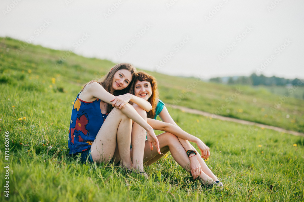 Two young lovely girls with long hair and naked legs spending time at nature outdoor. Women friendship. Weekend with beloved friend. Expressive emotion. Laughing and smiling teenagers. Youth lifestyle Two young lovely girls with long hair and naked legs spending time at nature outdoor. Women friendship. Weekend with beloved friend. Expressive emotion. Laughing and smiling teenagers. Youth lifestyle