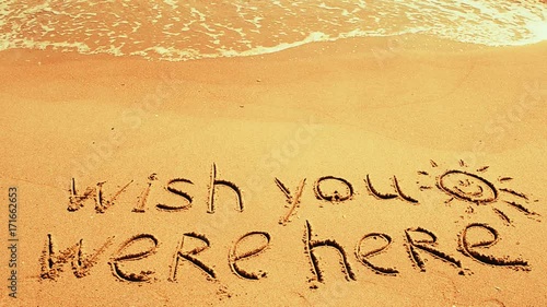 	Conceptual wish you were here text handwritten in sand on a beach