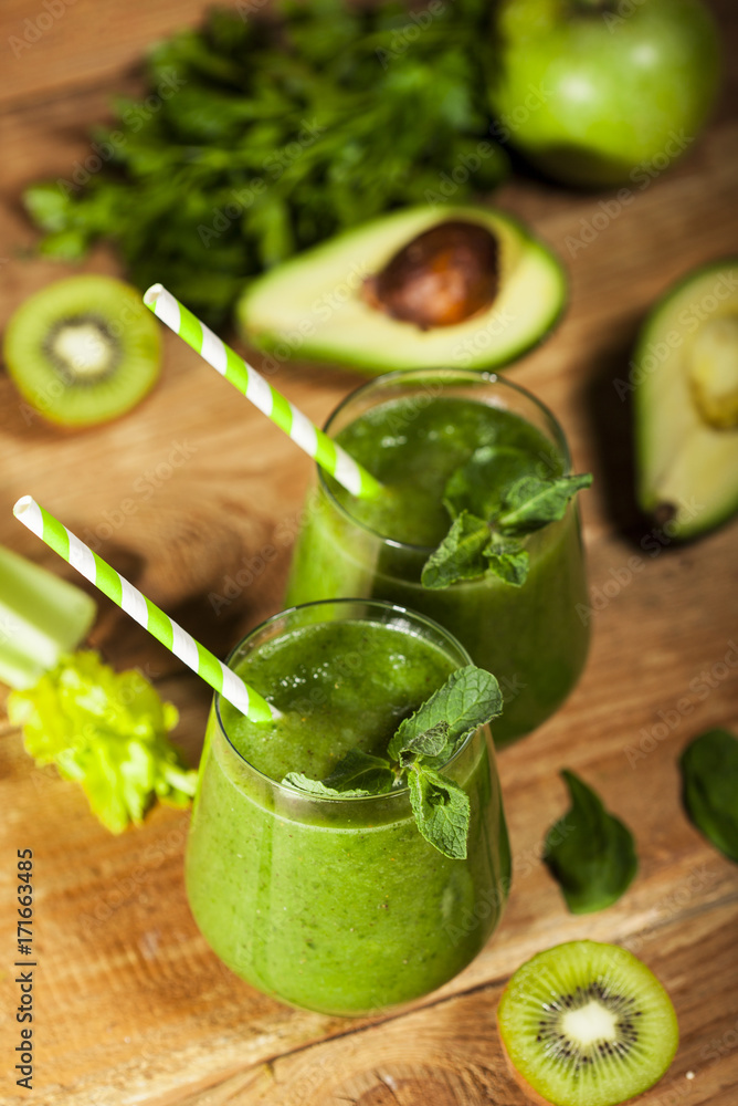 Freshly blended green smoothie in glasses with straws. Wooden background. Freshly blended green smoothie in glasses with straws. Wooden background.