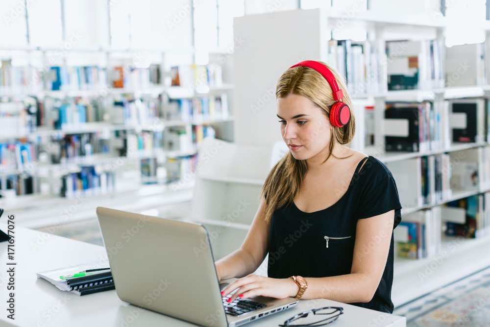 Portrait of a woman wearing red headphone using her laptop in a library. Portrait of a woman wearing red headphone using her laptop in a library.