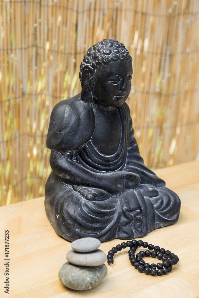 Buddha statue on a table with a mala and a bamboo background