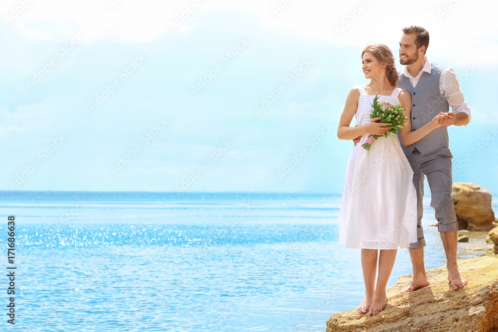 Newlywed couple standing on rocky beach