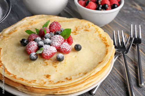 Stack of thin pancakes served with raspberry, black currant and sugar powder
