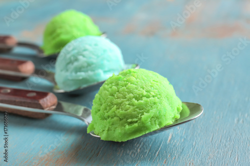 Green and blue scoops of ice-cream in spoons on wooden background