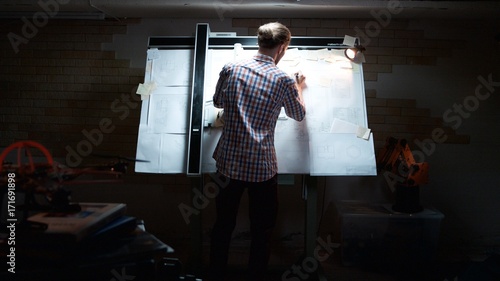 Rear view of male architect working on blueprint. Rear view of engineer drawing project of business district. Rear view of man engineer drawing photo