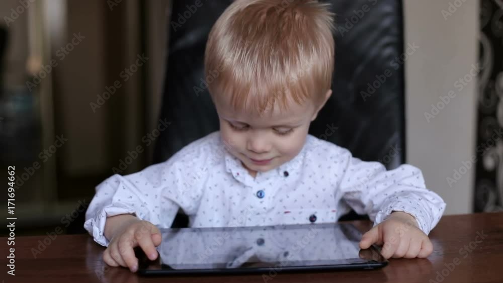 Portrait of little boy in a white shirt with tablet at the table. Portrait of little boy in a white shirt with tablet at the table.