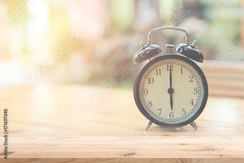 Retro clock at 6 o'clock on wood table foreground with blur light nature background
