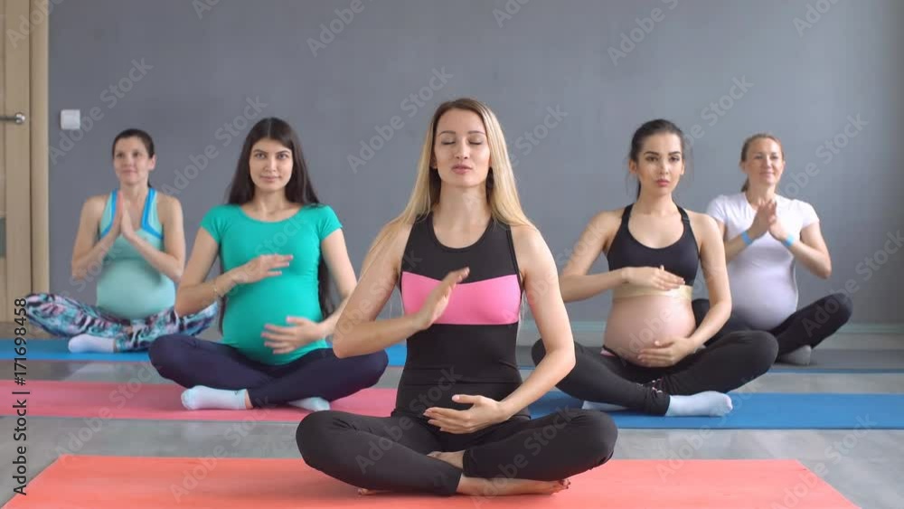 Pregnant woman practicing yoga along with a fitness instructor in the gym Pregnant woman practicing yoga along with a fitness instructor in the gym