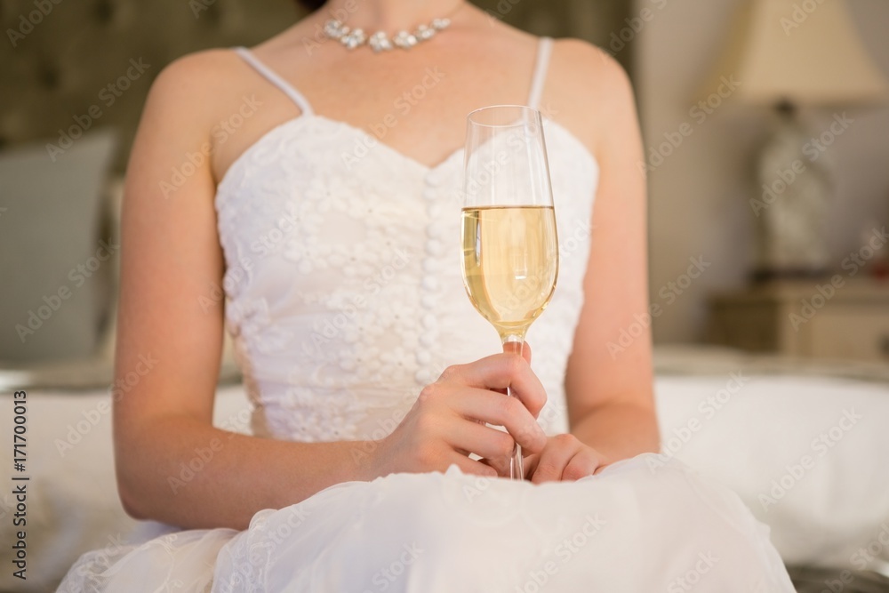 Midsection of bride holding champagne while sitting on bed Midsection of bride holding champagne while sitting on bed