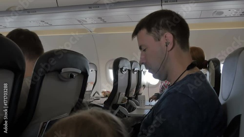 Young man listening to music on headphones via cell phone. A businessman during the flight is watching a video from a mobile phone, tablet. Business trip.