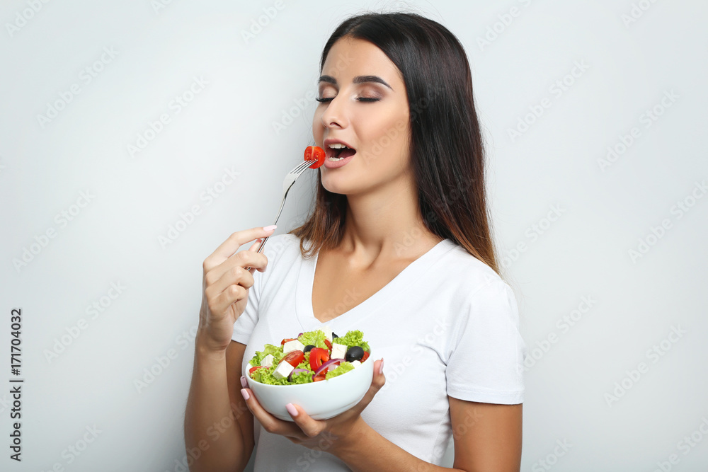 Young woman with vegetable salad in bowl on grey background Young woman with vegetable salad in bowl on grey background