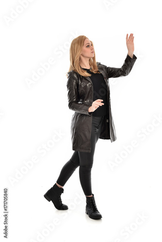 full length portrait of girl wearing black clothes and long leather jacket. standing pose in white background.