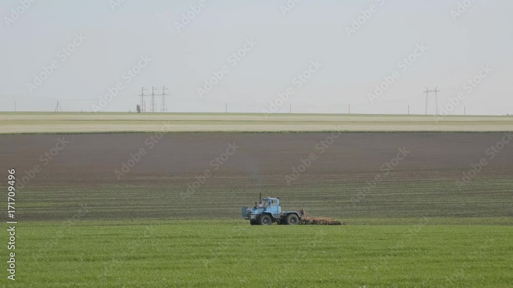 Blue wheeled tractor plowing a green field Blue wheeled tractor plowing a green field