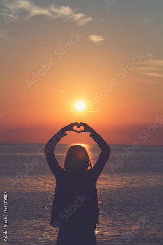 Silhouette of a girl holding a heart-shape with ocean / sea background.