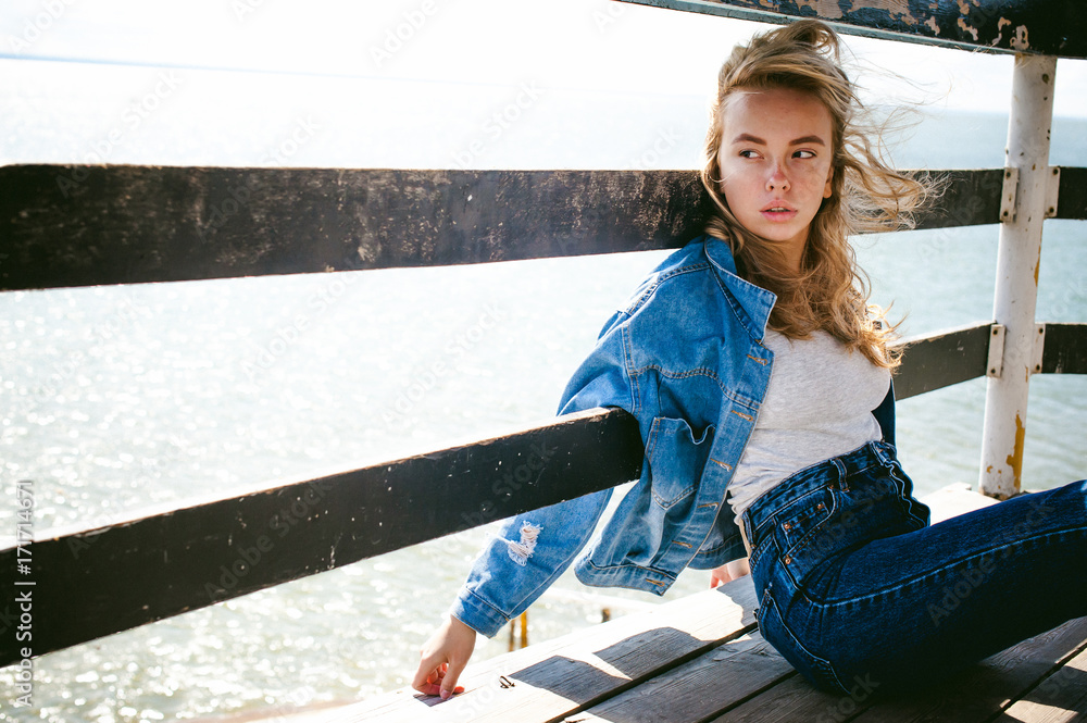 Obraz premium young beautiful woman in jeans clothes outdoors. portrait of a girl with freckles on her face, stylish girl on sea beach rescue tower, on a sunny summer autumn day.
