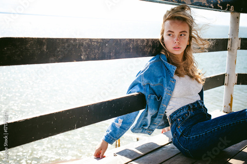young beautiful woman in jeans clothes outdoors. portrait of a girl with freckles on her face, stylish girl on sea beach rescue tower, on a sunny summer autumn day. photo