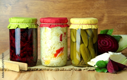 Preserved vegetables. Beetroot, cabbage and cucumbers in a glass jars. Wooden background.