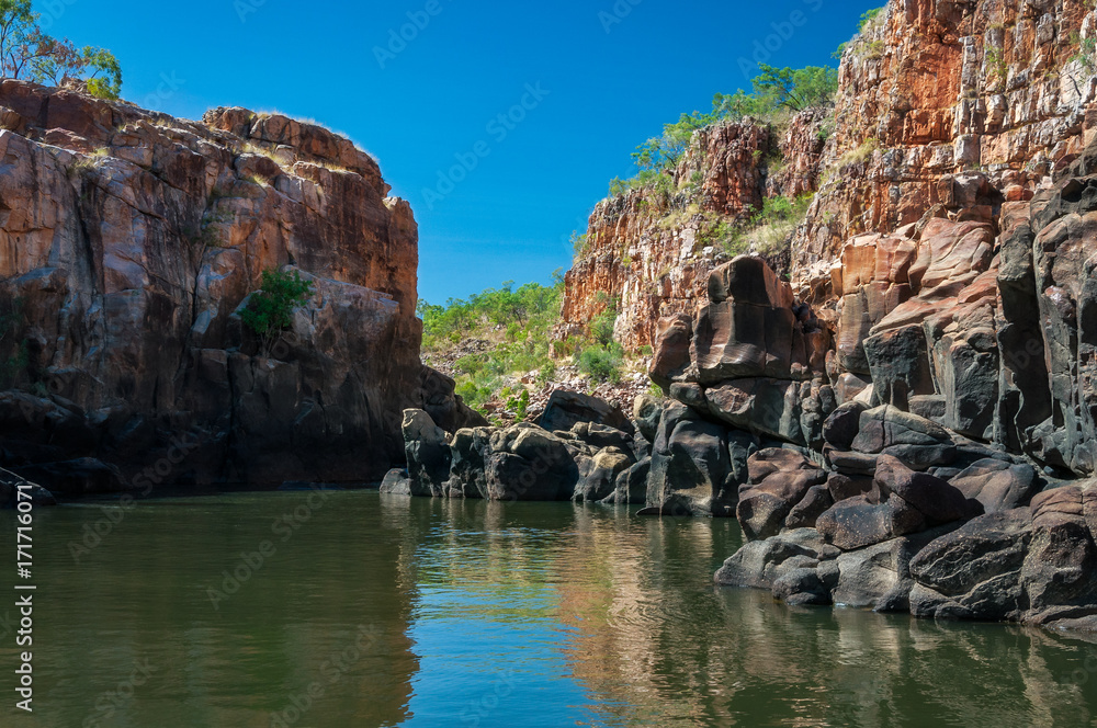 Rocky cliff face with reflections on the Katherine River banks, the end point of the cruise tour in the dry season at Katherine Gorge in Nitmiluk National Park, Northern Territory, Australia.