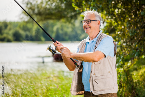 Happy senior man is fishing on sunny day.