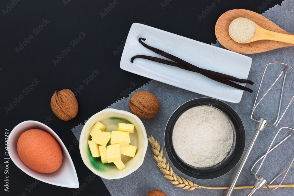 Food concept Bakery preparation by flour, egg, butter, sugar, chocolate, vanilla beans, walnuts and milk decor by wheat ear on bake paper and black background Food concept Bakery preparation by flour, egg, butter, sugar, chocolate, vanilla beans, walnuts and milk decor by wheat ear on bake paper and black background