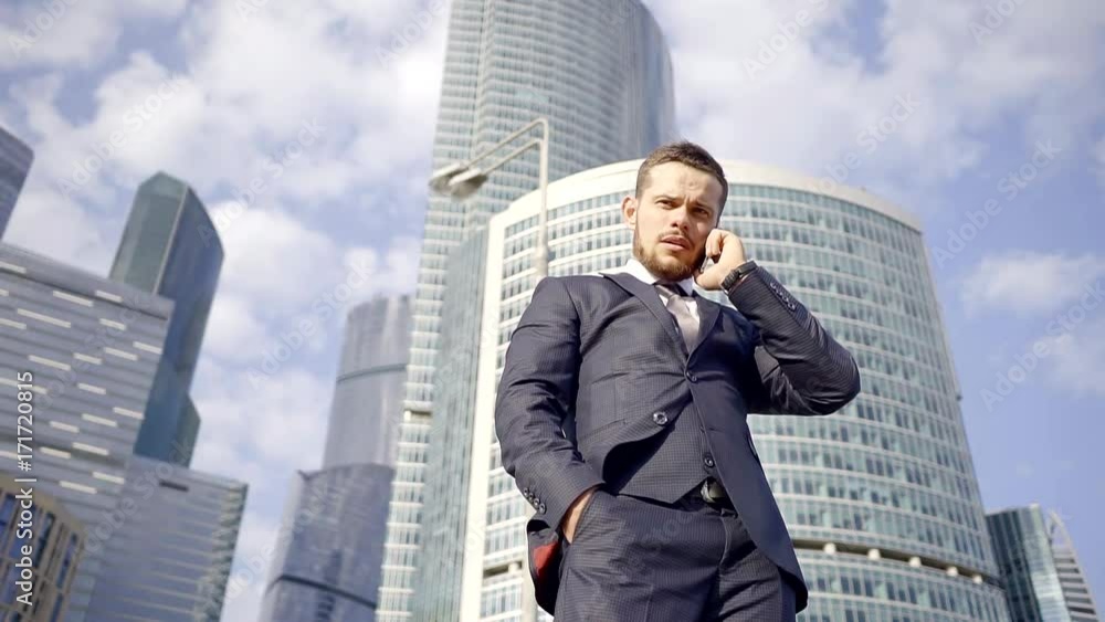 handsome fashion man is speaking by telephone, standing in outdoors in sunny day handsome fashion man is speaking by telephone, standing in outdoors in sunny day