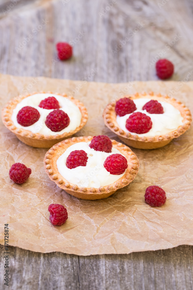 Sweet Tartlets With Cream And Fresh Raspberries On Crumpled Sheet Of Paper On Wooden Background Top View. Sweet Tartlets With Cream And Fresh Raspberries On Crumpled Sheet Of Paper On Wooden Background Top View.