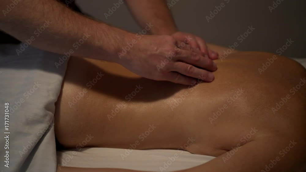 Medium tight shot of a mature caucasian woman getting a massage by a man using two large smooth black stones in a circular motion. Woman has smile on her face and is topless. Medium tight shot of a mature caucasian woman getting a massage by a man using two large smooth black stones in a circular motion. Woman has smile on her face and is topless.