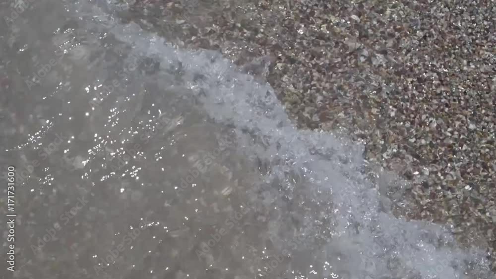 A wave on the sea carries away a wave of small stones and sand on the seashore A wave on the sea carries away a wave of small stones and sand on the seashore