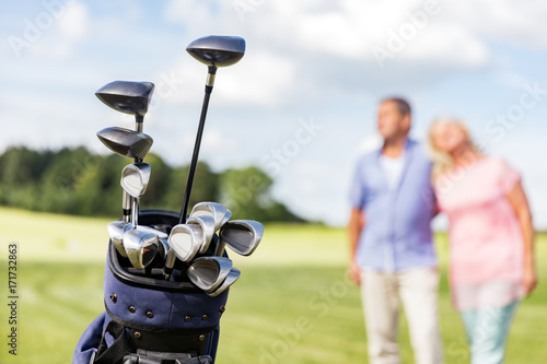 Set of golf clubs with senior couple in the background.