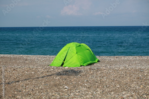 A green tent is on a pebbly beach by the sea
