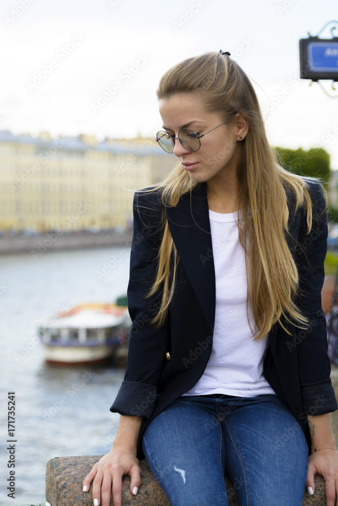 Beautiful blonde girl, dressed with a dark jacket, standing in a bridge. Sankt-petersburg