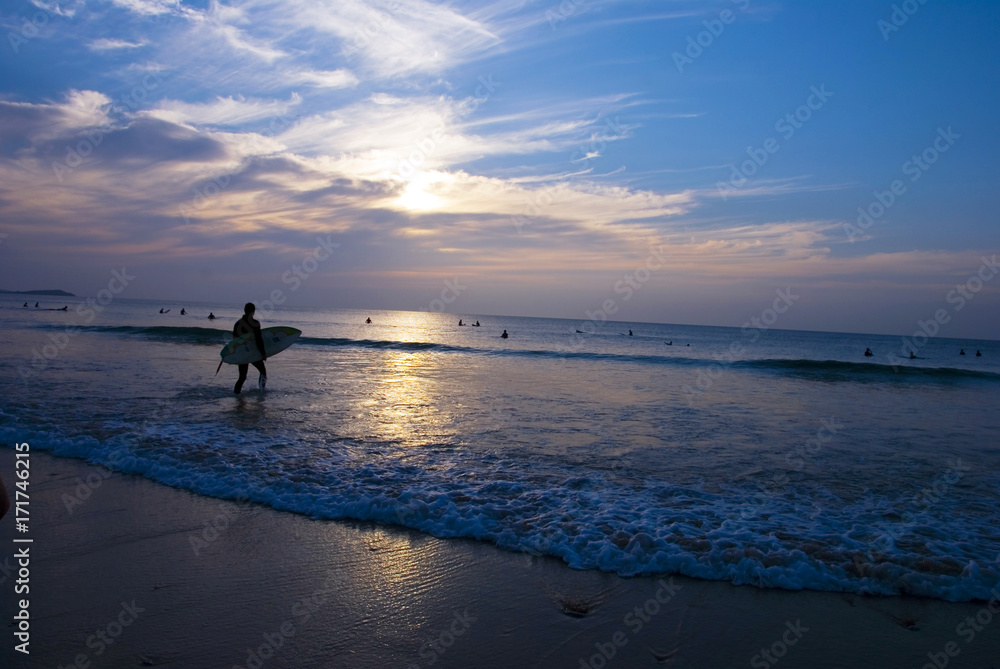 Surfer with Surfboard walking into the sea at sunset