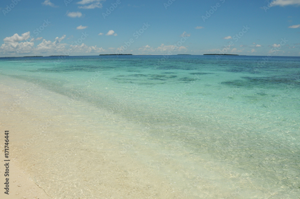 Crystal clear blue waters of the Indian Ocean, view from beach on golden sands in the Maldives