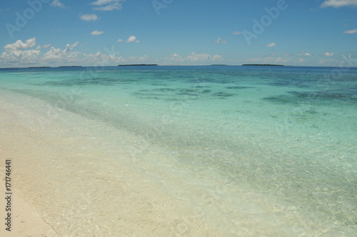 Crystal clear blue waters of the Indian Ocean, view from beach on golden sands in the Maldives